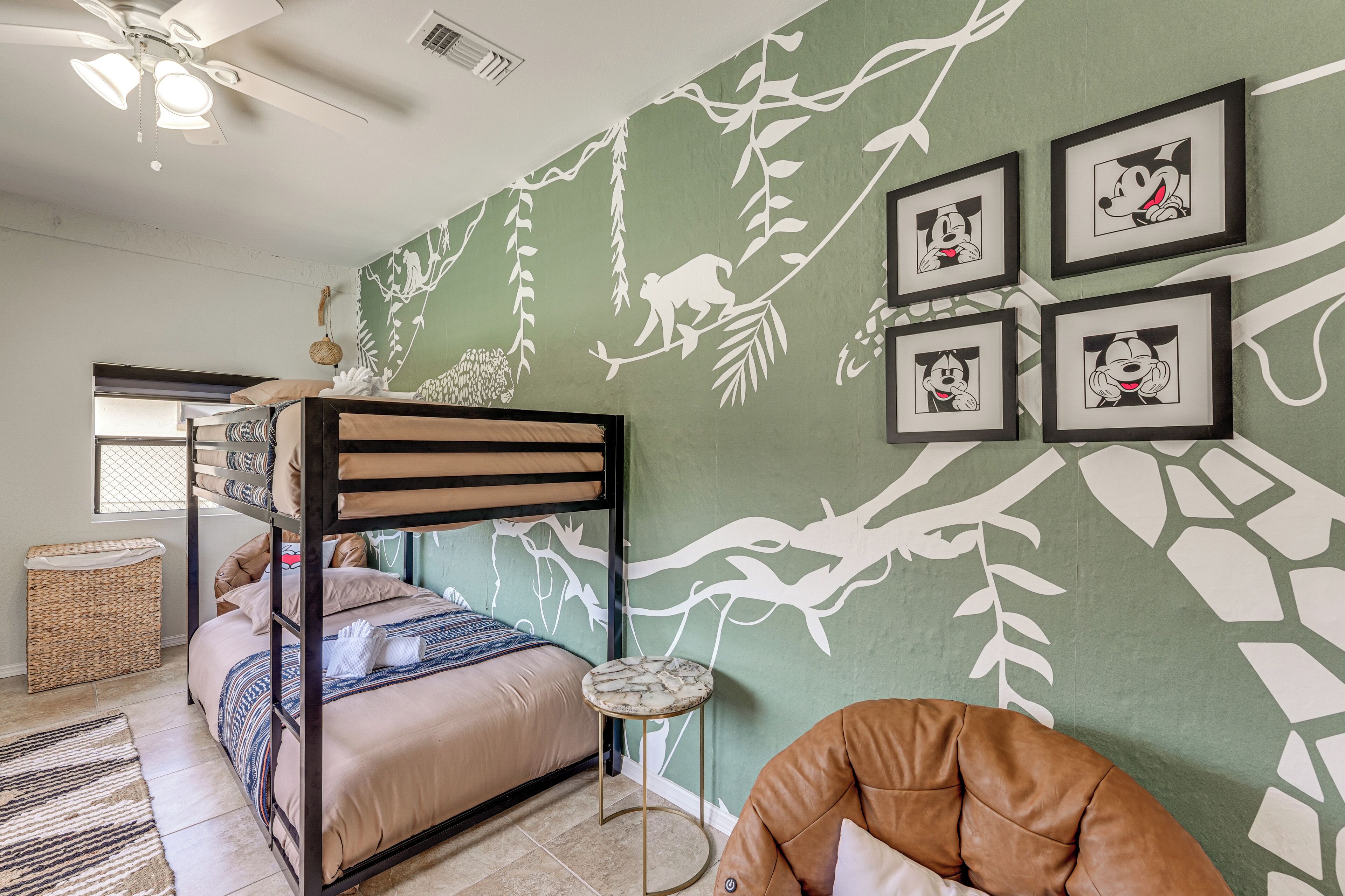 A room with a bunk bed, a round side table, a hanging plant, and framed pictures on the wall.