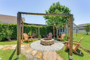 Ein Garten mit einem Steinkamin, Holzstühlen und einer Holzpergola.