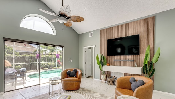 A modern living room with a large TV, comfortable seating, a ceiling fan, and a view of a swimming pool. - Disney Getaway w/ Private Hot Tub 14 Mi to Parks (Kissimmee)