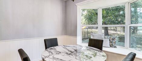 A dining area with a marble table, black chairs, a chandelier, and a view through large windows.