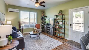 A living room with a sofa, coffee table, and fireplace. There is a ceiling fan, a window with blinds, and a door with a glass panel.