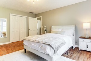 Un dormitorio con una cama grande, paredes blancas, suelo de madera, una mesita de noche y una puerta.
