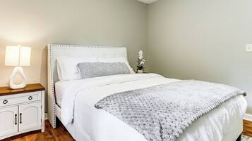 A neatly made bed with a white headboard, a grey blanket, and a bedside table with a lamp.