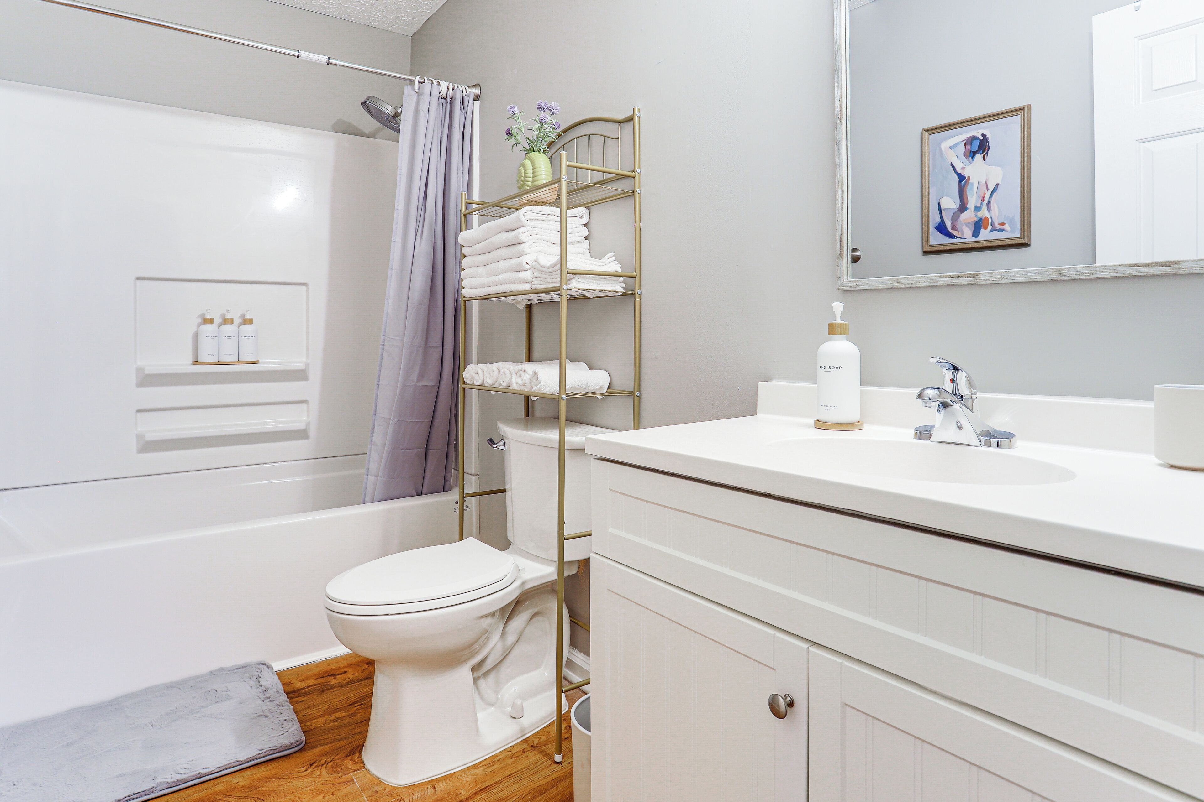 A bathroom with a white toilet, a shower area, a towel rack, a sink with a mirror, and toiletries on the wall.