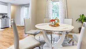 A dining area with a round table, four chairs, and a vase with flowers.