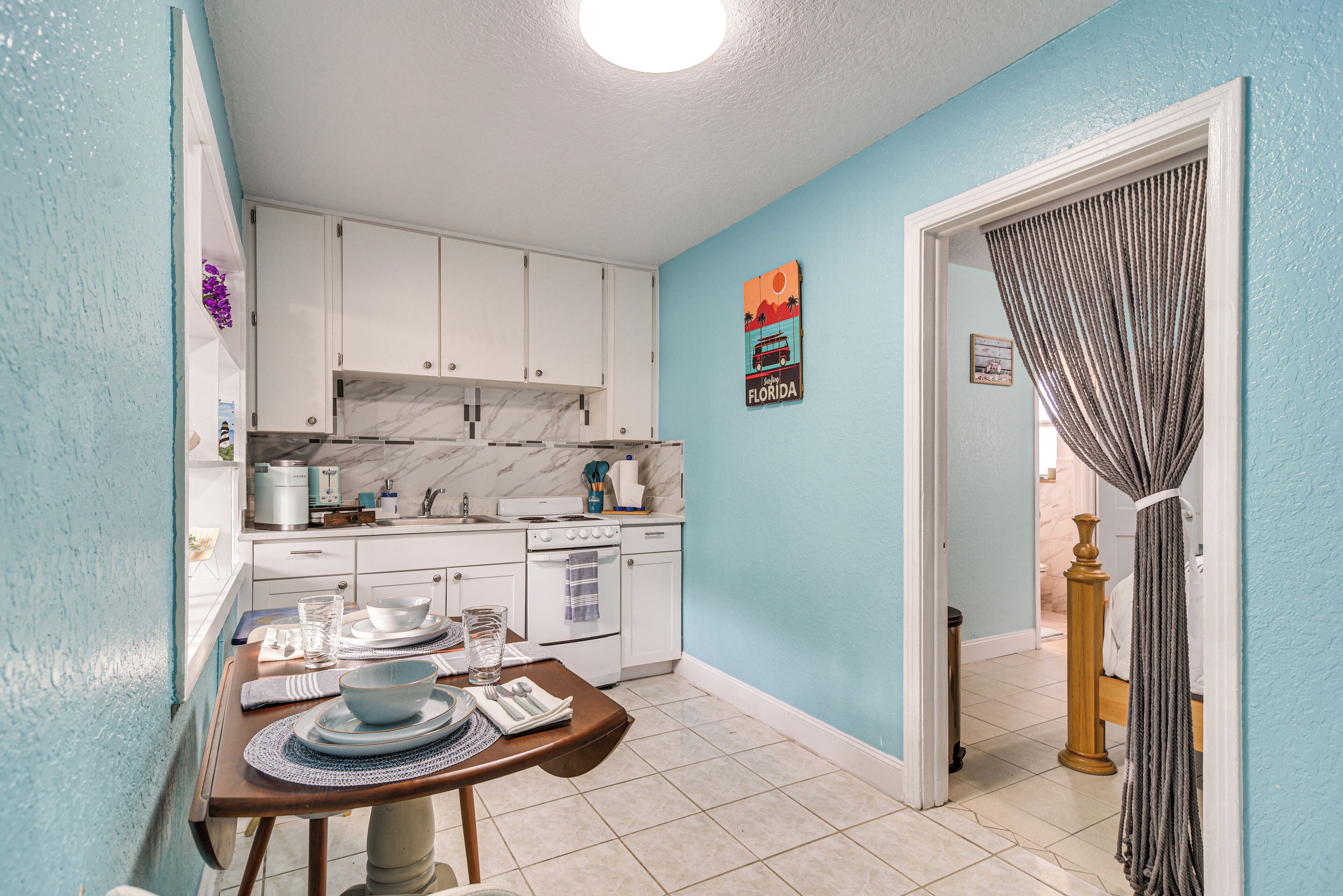 A compact kitchen with white cabinets, a marble backsplash, and a dining area with a table set for two.