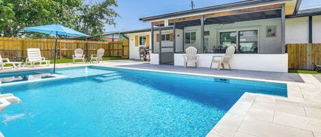 A swimming pool with a patio area, outdoor seating, and a covered section with a grill.
