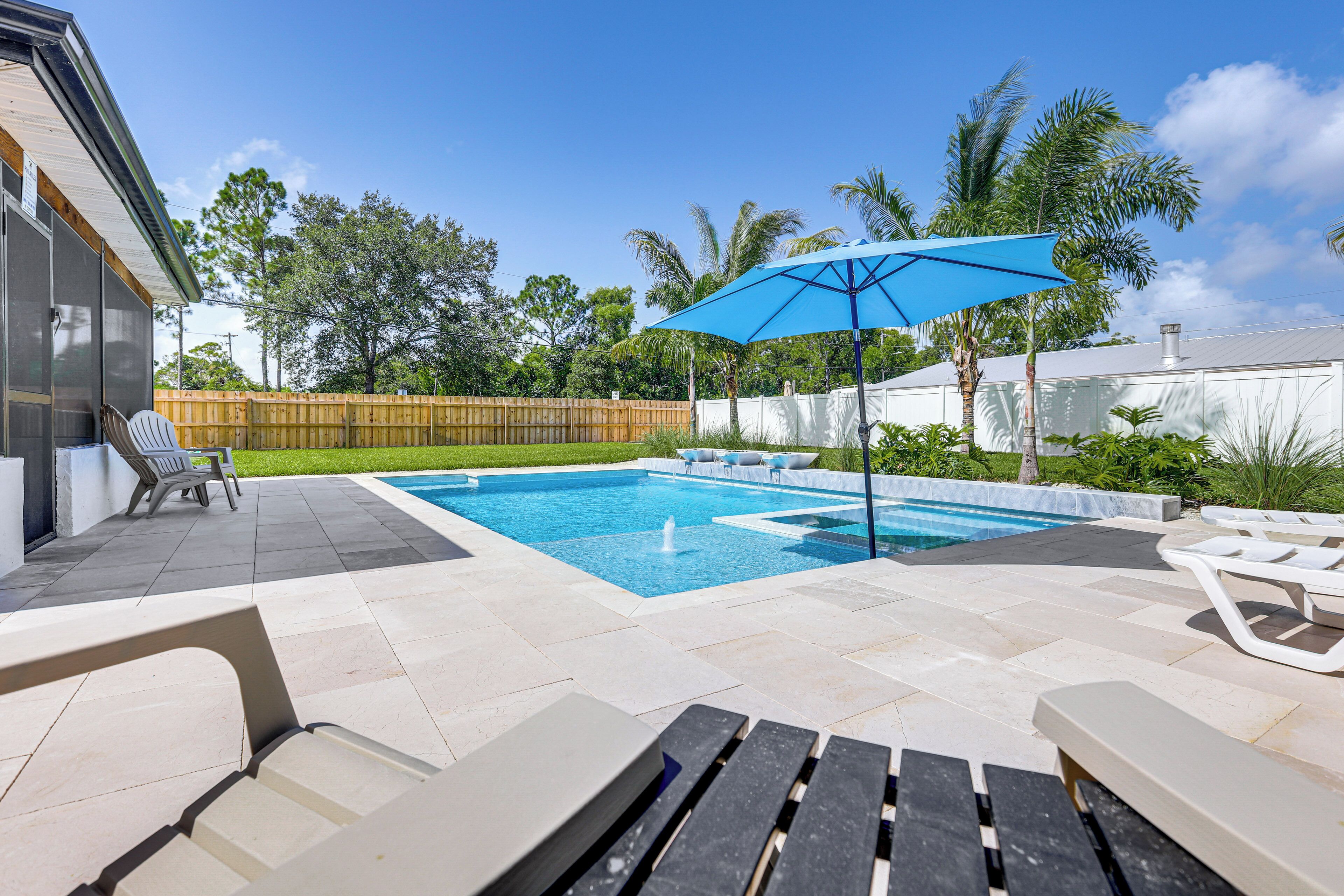 A backyard with a swimming pool, lounge chairs, and a wooden fence.
