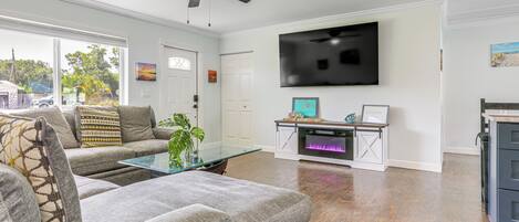 A living room with a grey sofa, a glass coffee table, a ceiling fan, a flat-screen TV, and a fireplace.