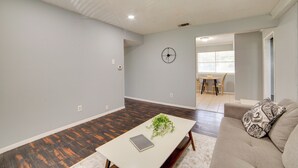 Un salon spacieux avec une table basse blanche, un canapé beige et un coin repas à l’arrière-plan.