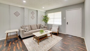 Un salon avec un canapé, une table basse, un fauteuil, une plante et une porte.