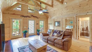 A cozy wooden cabin interior with a leather sofa, a wooden coffee table, and a ceiling fan. - Updated Cabin By Linville Falls: Deck & Game Room! (Marion)