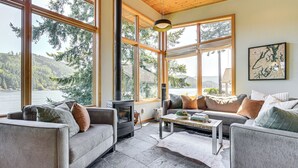 A cozy living room with large windows, a fireplace, and a comfortable seating area. - Modern Summit Lake Escape - Spacious Deck w/ View! (Olympia)