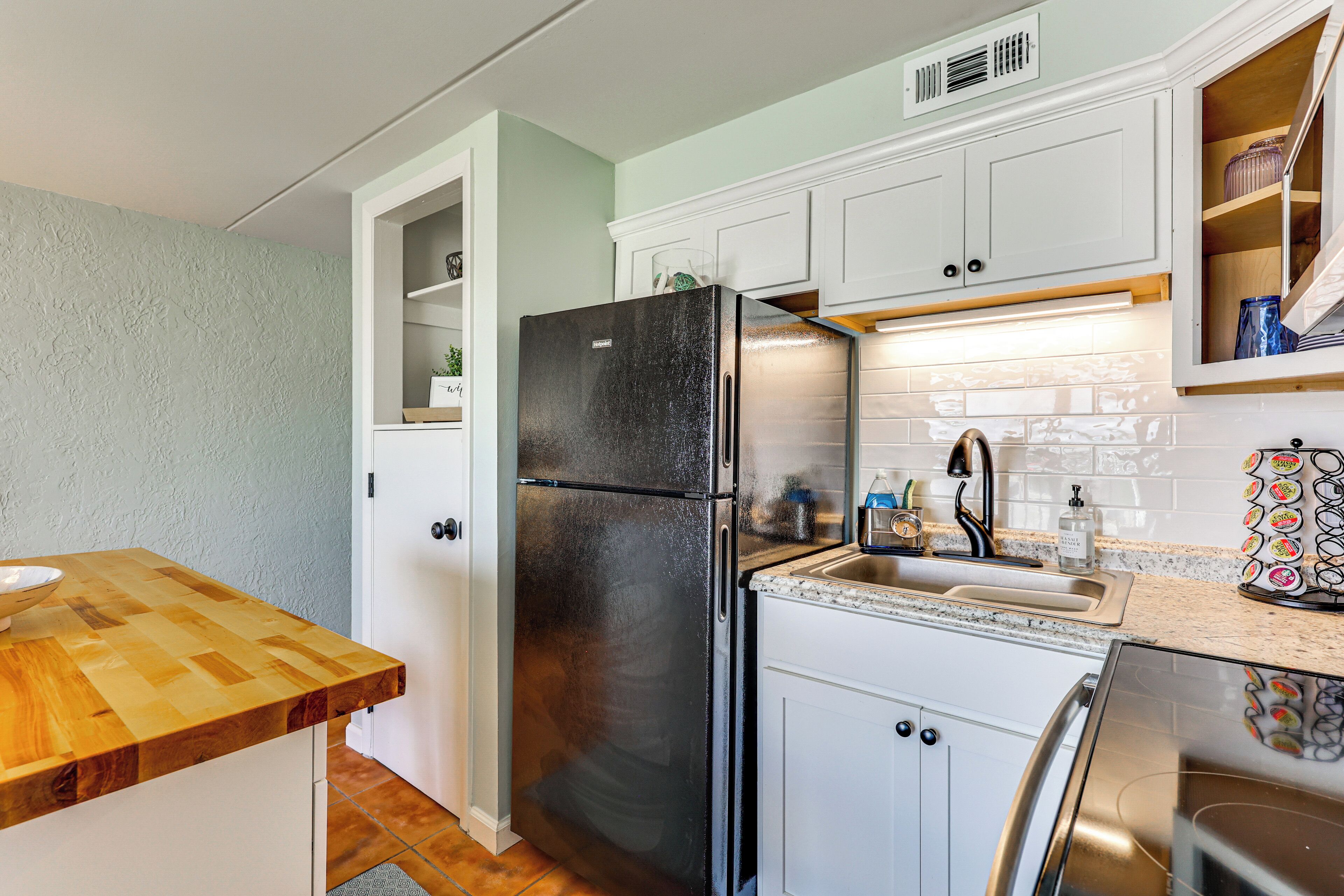 Una cocina con armarios blancos, un refrigerador negro, una encimera de madera y un fregadero de acero inoxidable.