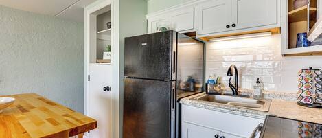 Una cocina con armarios blancos, un refrigerador negro, una encimera de madera y un fregadero de acero inoxidable.