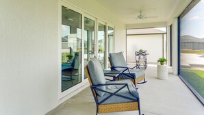 A covered patio area with wicker chairs and a table, large sliding glass doors, and a ceiling fan.