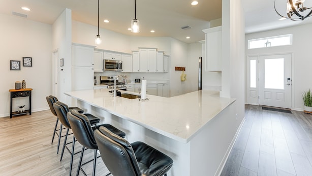 A modern kitchen with white cabinets, a large island with bar stools, stainless steel appliances, and pendant lighting.
