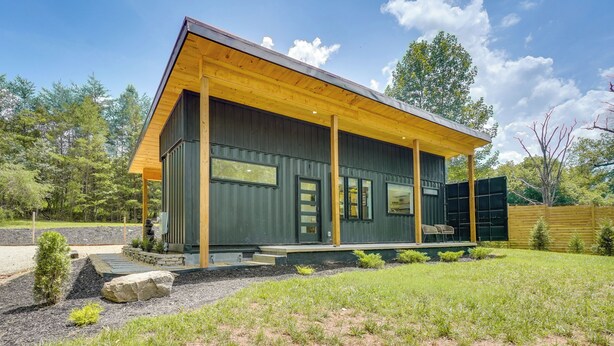 A modern house with a covered porch, large windows, and a well-maintained lawn.