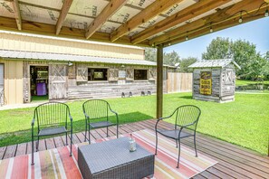 Eine Außenpatio mit Tisch und Stühlen, ein kleines Gartenhaus mit Schild, und ein Gebäude mit Wellblechdach.