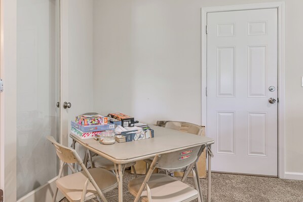 A room with a white door, a table with chairs, and various items on the table including boxes and a jar.