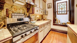 A kitchen with a gas stove, white cabinets, a microwave, and a stained glass window. - Vintage Studio in Historic Dtwn La Porte! (La Porte)