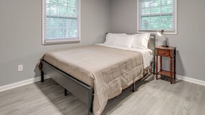 A bedroom with a bed, two windows, a nightstand, and a lamp.