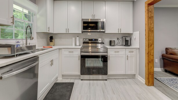 A modern kitchen with white cabinets, stainless steel appliances, and a window with a view of greenery.