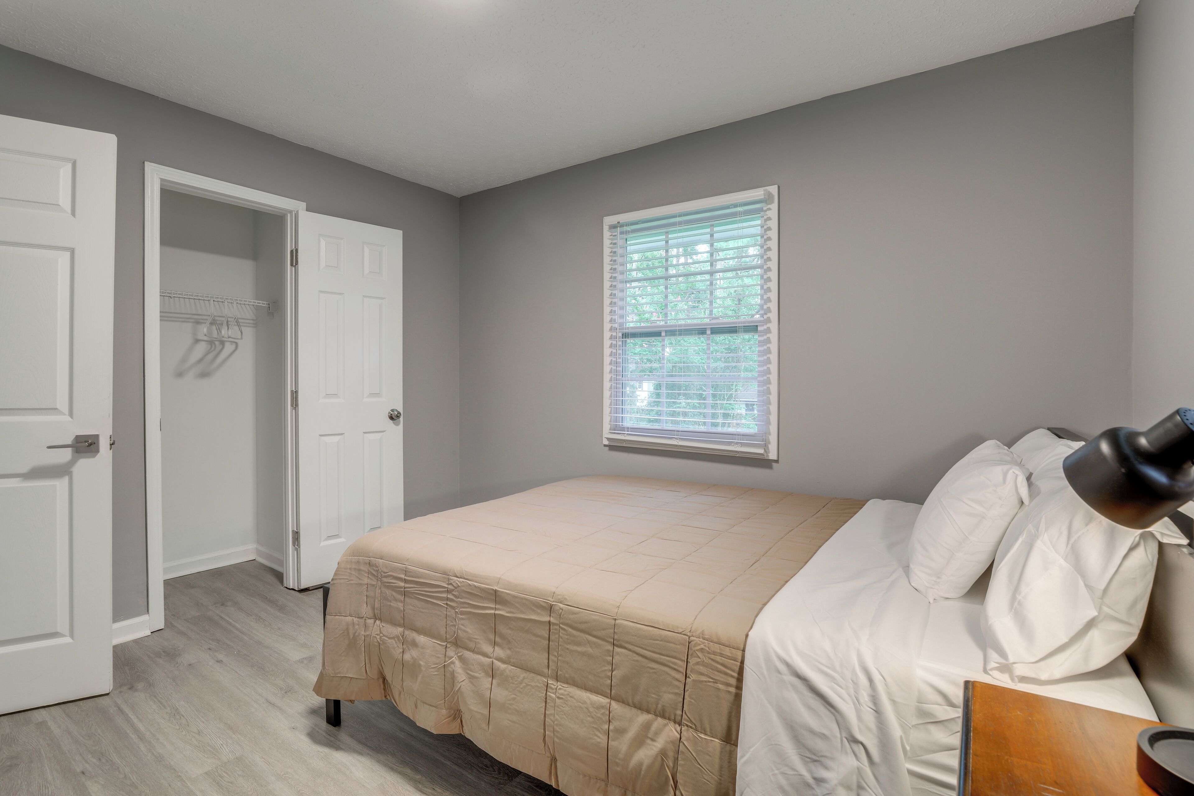 Um quarto com cama, janela com persianas, porta e um cabideiro.