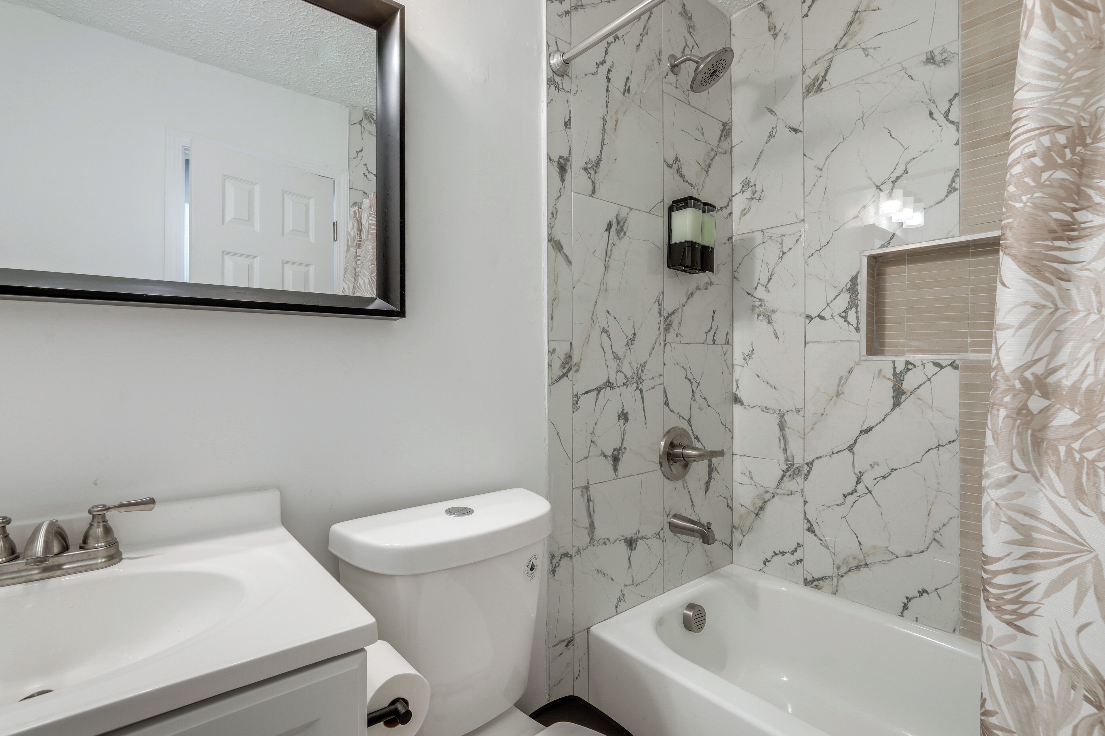 A bathroom with a white sink, toilet, and bathtub, marble walls, and a shower area.