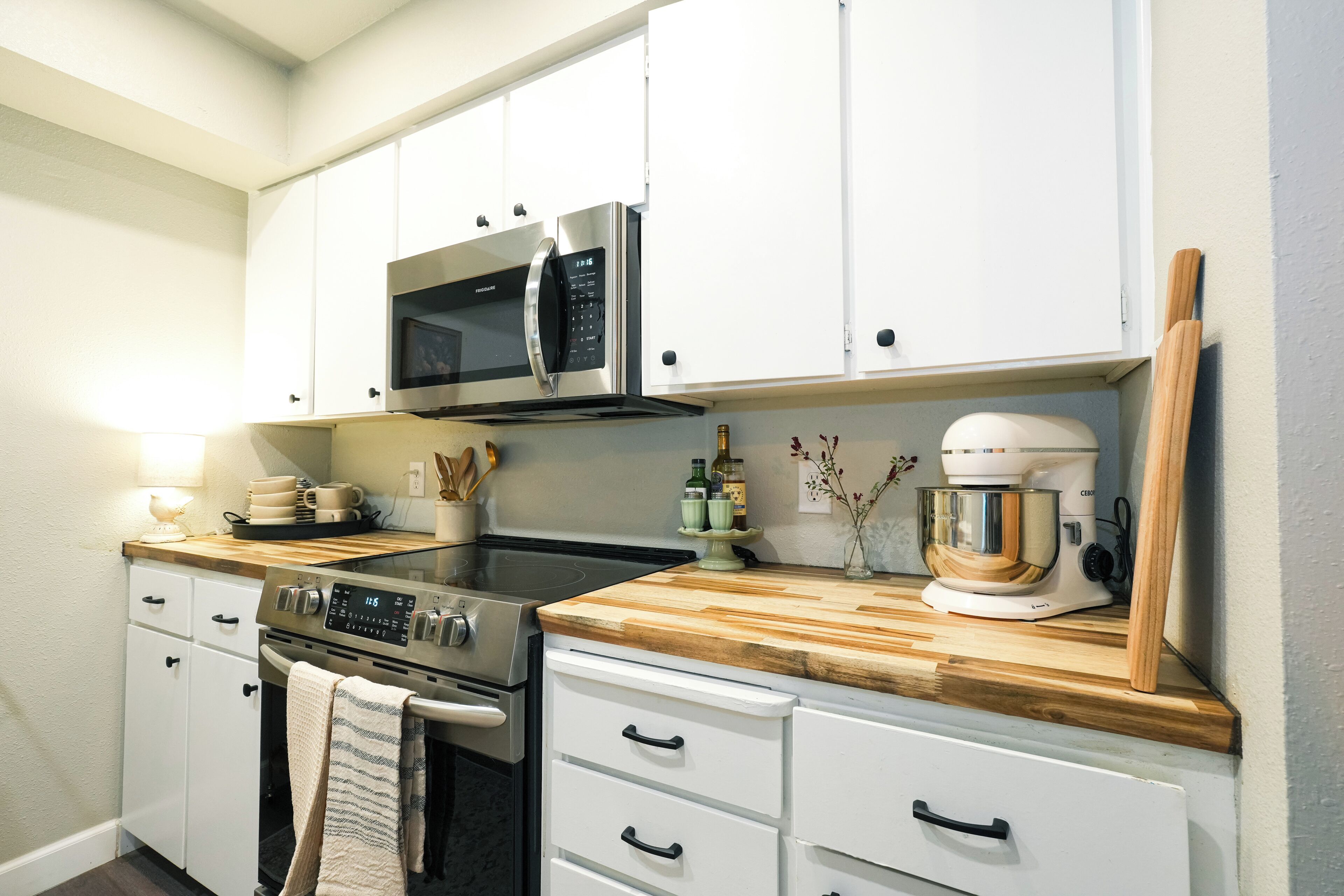 A modern kitchen with white cabinets, stainless steel appliances, and wooden countertops.