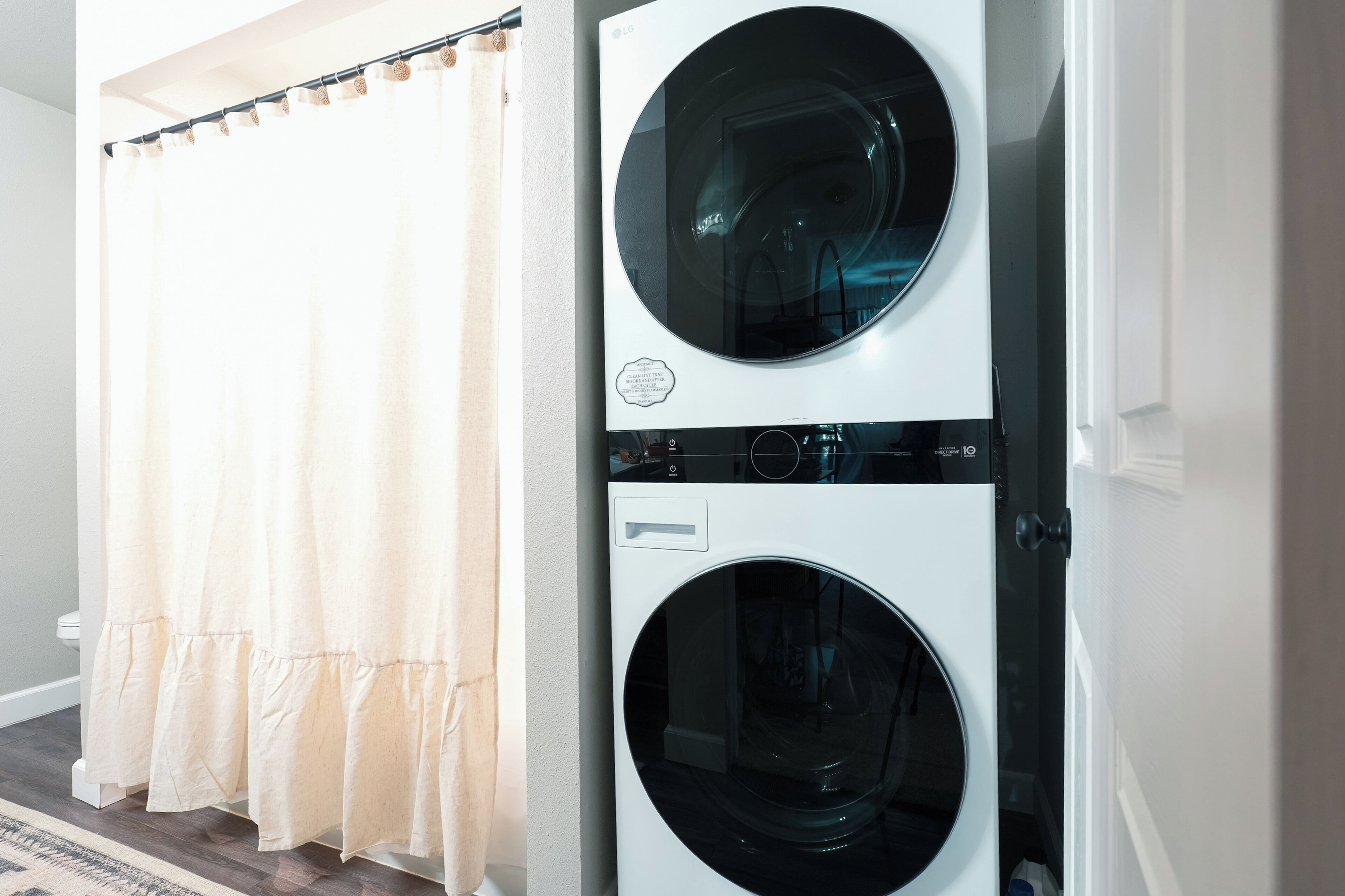 A laundry area with two stacked front-loading washing machines and a beige curtain.