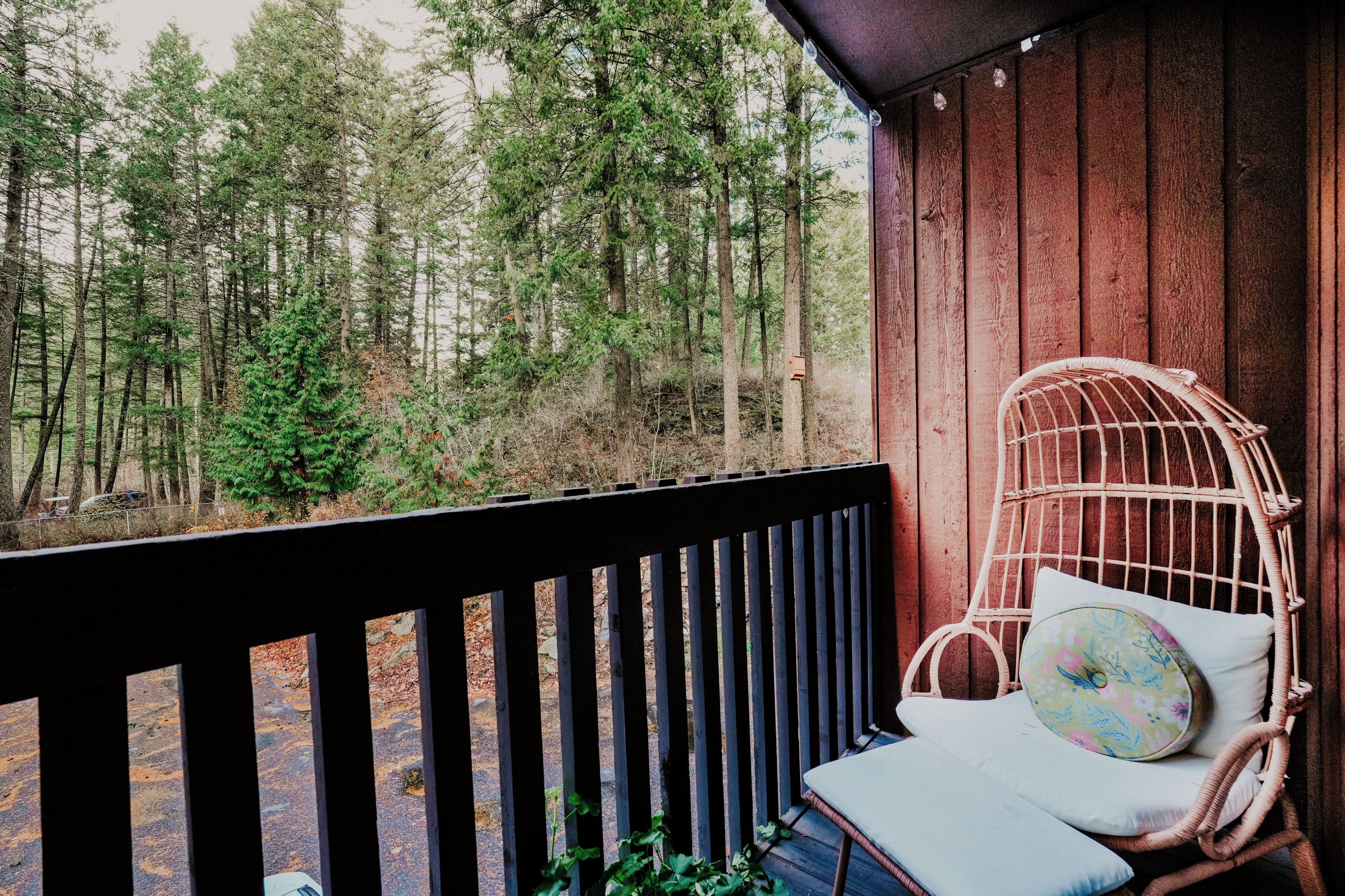 Une terrasse en bois avec une chaise en osier et des coussins, donnant sur une forêt.