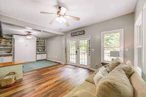 Ein geräumiges Wohnzimmer mit beigefarbenem Sofa, Holzböden, Deckenventilatoren und einer Küchenzeile mit weißen Schränken und Regalen.