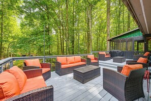 Eine Terrass mit Korbmöbeln und orangefarbenen Kissen, umgeben von einem Wald.