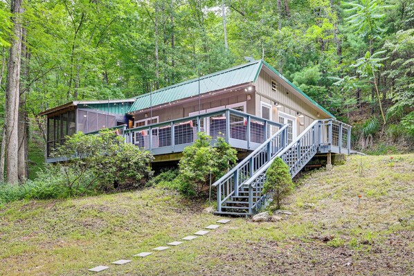 Eine Hütte mit einer Metalltreppe, die zu einer Terrasse führt, umgeben von dichtem Wald.