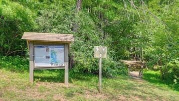 A wooden signpost with hiking and cycling symbols, a small shelter with a bulletin board, and a dirt path leading into a wooded area.