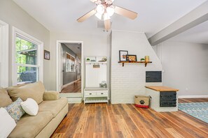 Ein gemütliches Wohnzimmer mit einem beigefarbenen Sofa, Holzböden, einem Deckenventilator und einer Tierbox.