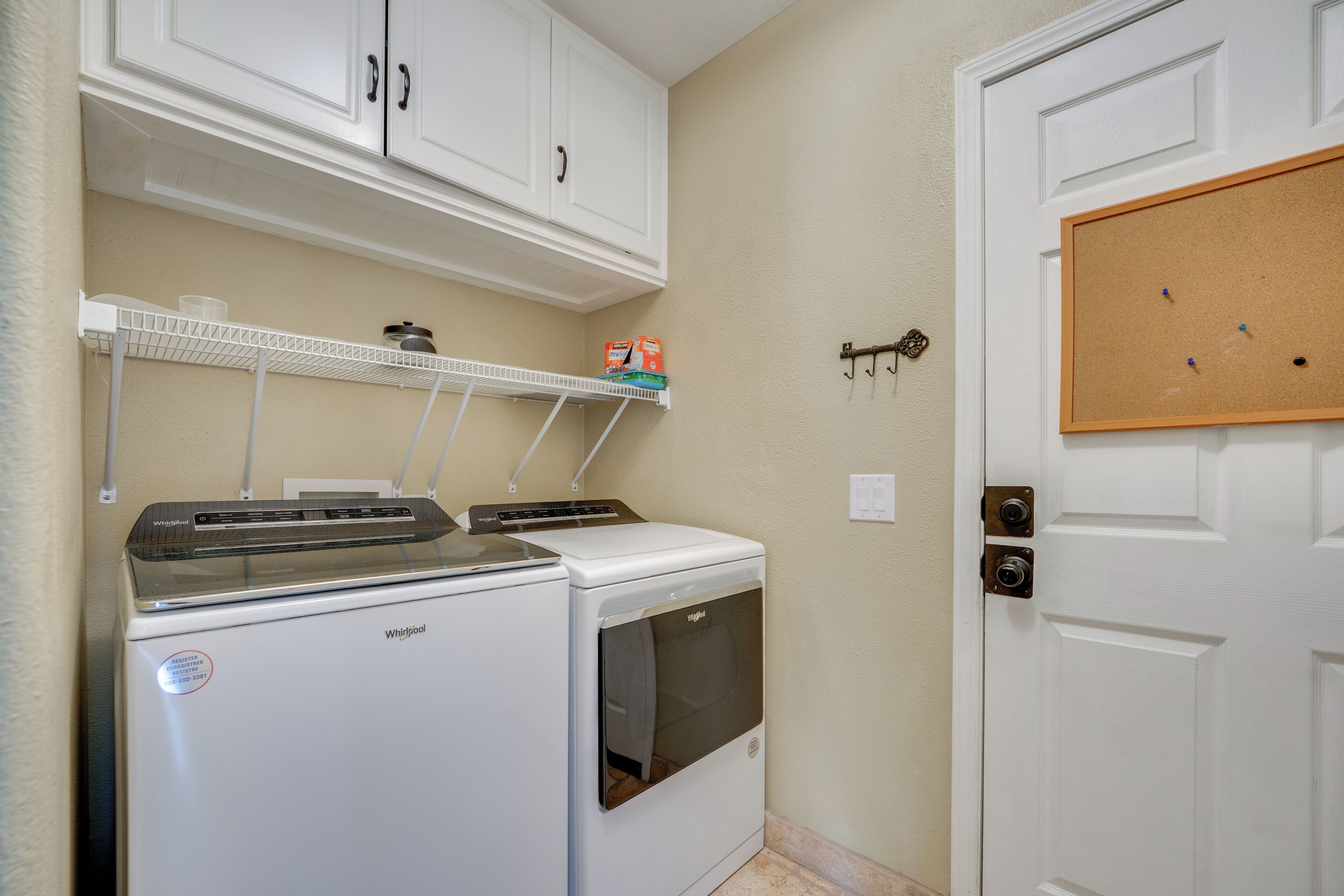 A laundry room with a washer and dryer, a shelf with cleaning supplies, and a corkboard on the wall.