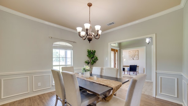 A dining area with a dark wooden table, beige upholstered chairs, a woven placemat, and a chandelier.