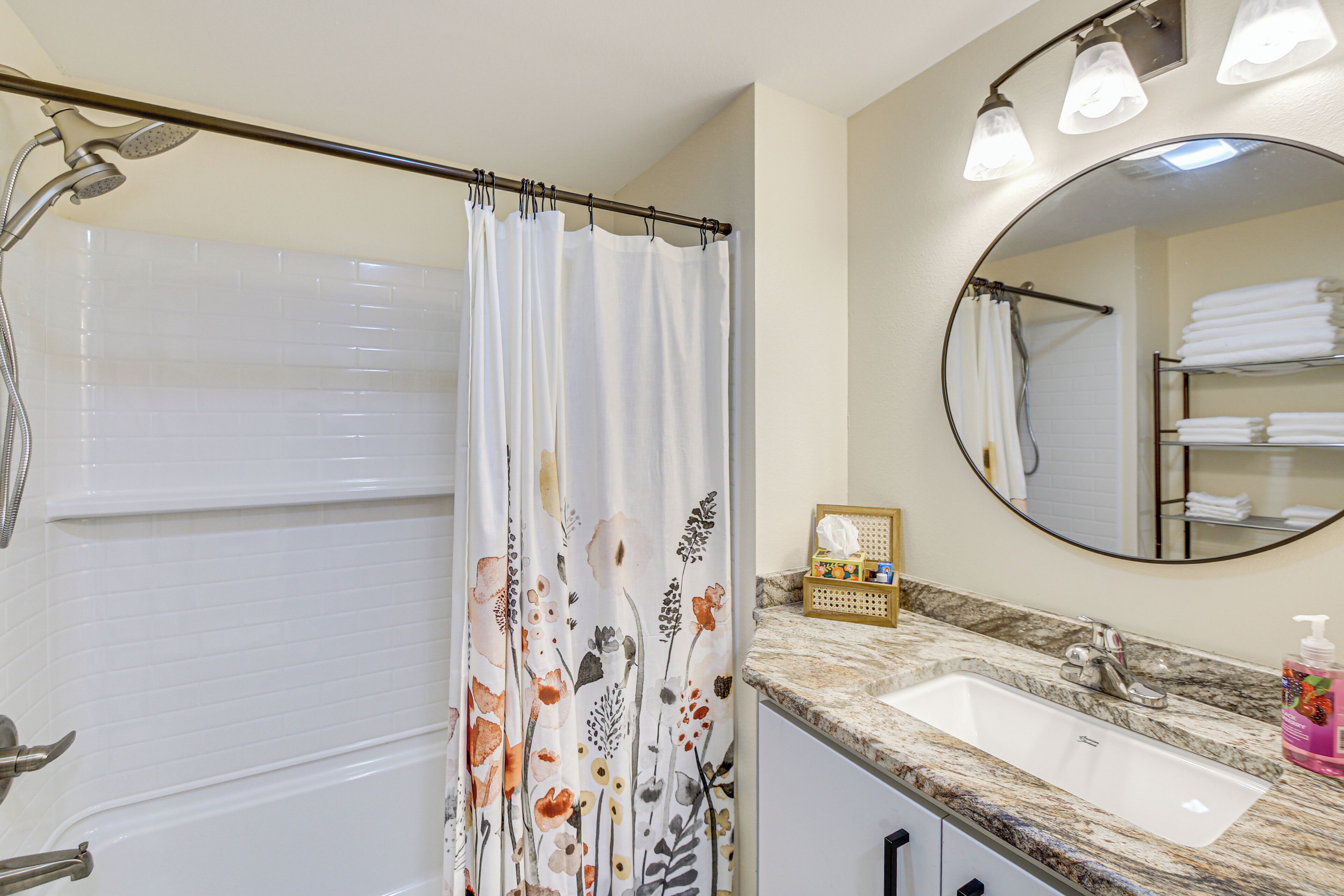 A bathroom with a shower, a sink, a mirror, and a towel rack.
