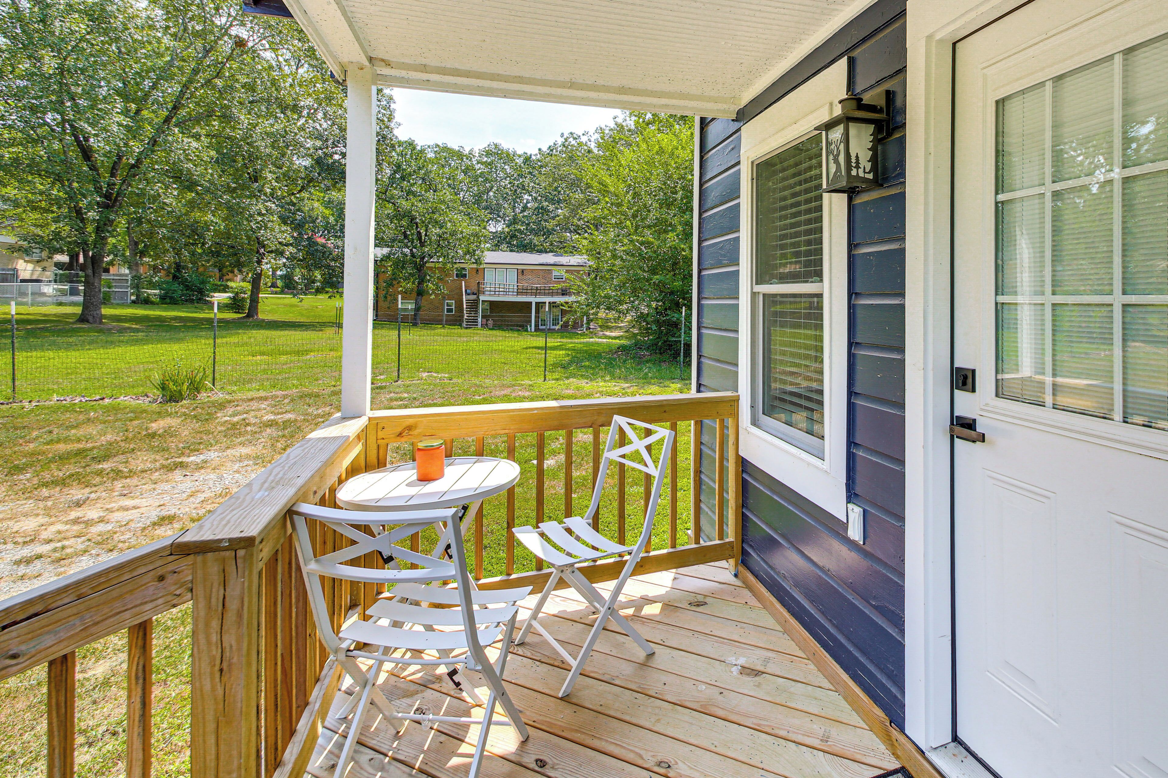 A wooden deck with a table and chairs, a white door, and a view of a grassy yard and trees.