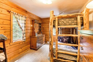 A rustic wooden cabin room with a bunk bed, a dresser, and a window with a plaid curtain. - Private Hannibal Cabin With Sauna & Hot Tub! (Hannibal)