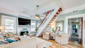 Un vaste salon doté d’un escalier en bois, d’une cheminée et d’un téléviseur fixé au mur.