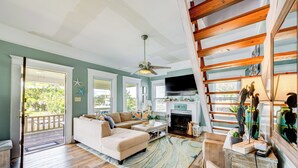 Un salon spacieux avec un canapé, une table basse et une cheminée. On y trouve un escalier avec des rampes en bois et un téléviseur fixé au mur.