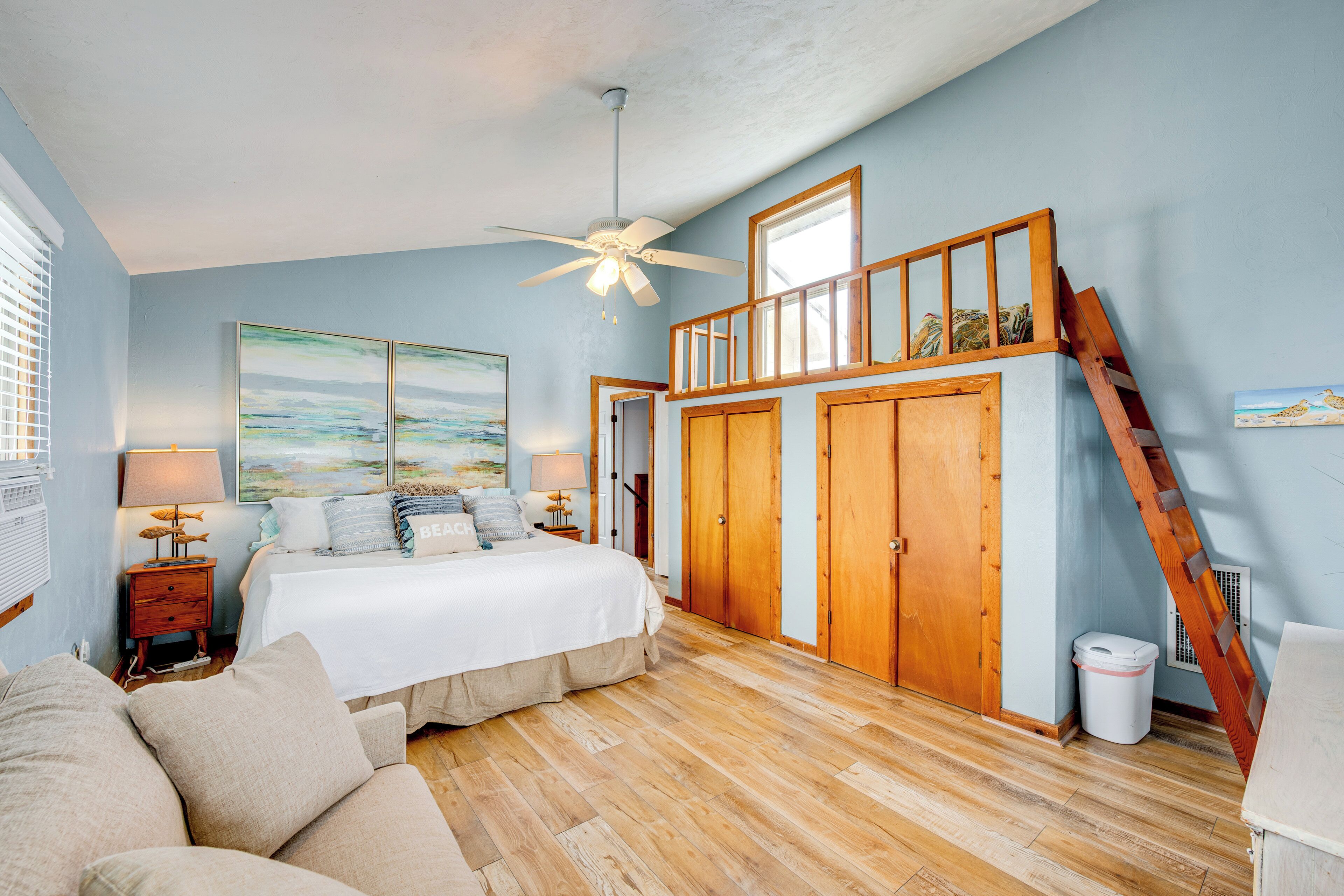 A bedroom with a bed, wooden floor, ceiling fan, and a loft area with a ladder.