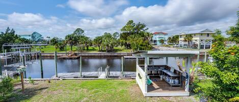 A waterfront property with a dock, a covered outdoor seating area, and a view of the water and surrounding greenery.
