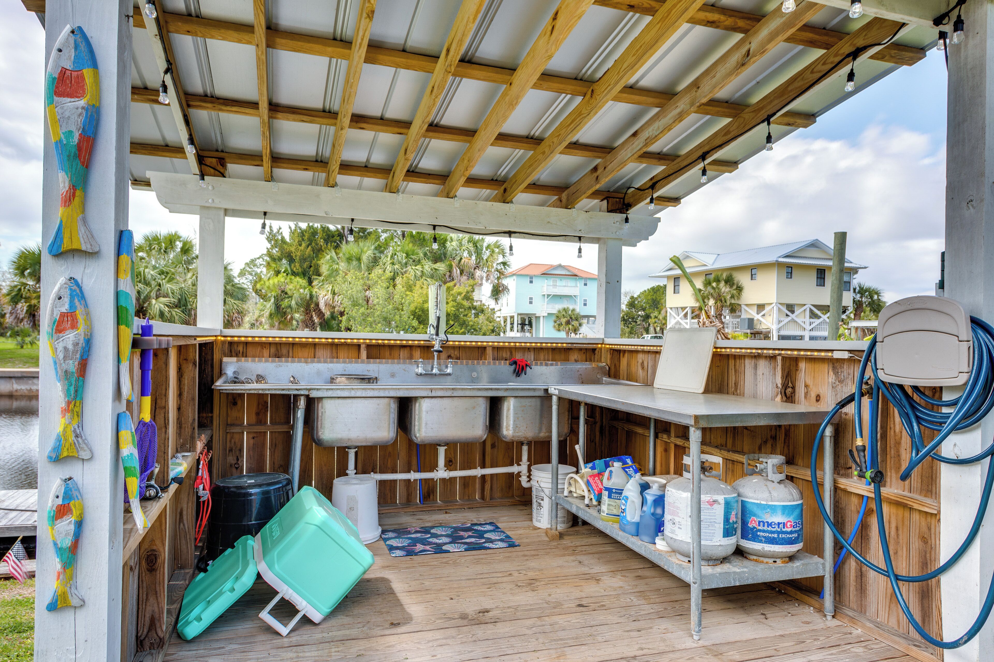 Une cuisine extérieure abritée, dotée d’une terrasse en bois, d’éviers en métal et d’étagères de rangement.