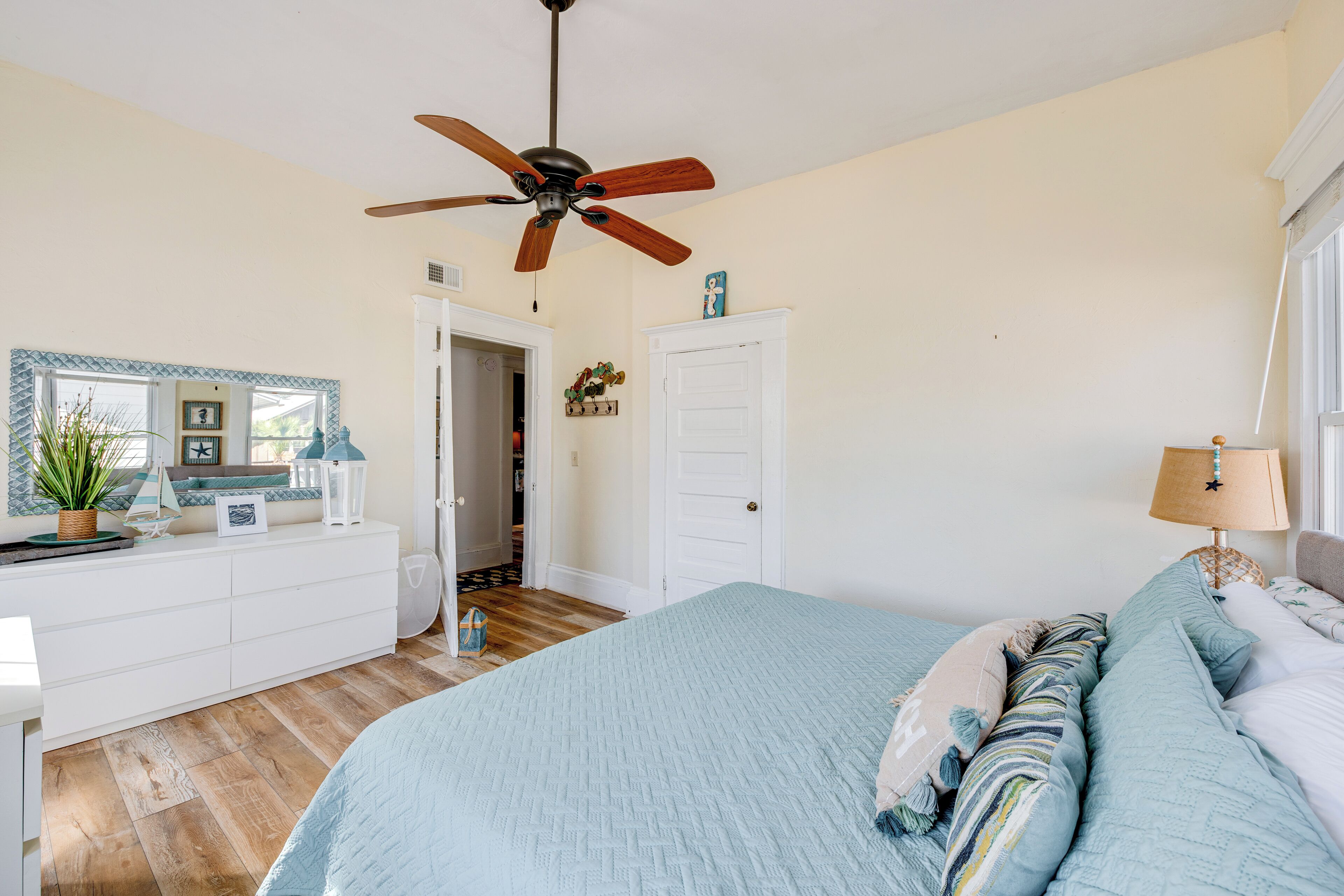 A bedroom with a bed, a dresser, a ceiling fan, and a door leading to another room.