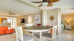 Een eetruimte met een ronde tafel en witte stoelen, een plafondventilator en een keuken op de achtergrond.
