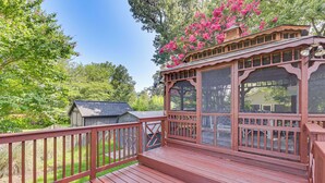 A wooden deck with a covered area, surrounded by greenery and a small shed. - Fish, Swim & Boat: Colonial Beach Bungalow (Colonial Beach)